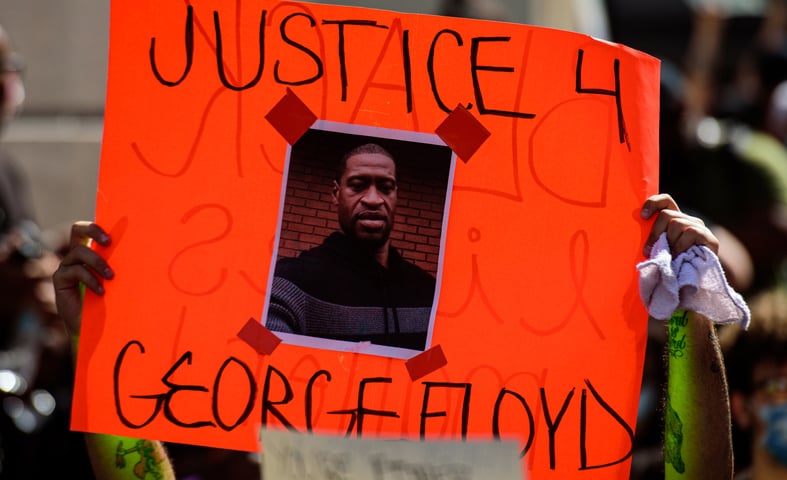 A person holding up an orange sign with the image of George Floyd with the words Justice 4 George Floyd on it 