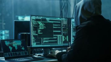 An image featuring a person using his computer and laptop for hacking representing a cybercrime hacker